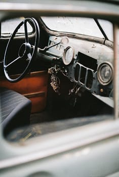 Interior of vintage automobile with steering wheel and speedometer with arrow on rusty surface near wire bundle in daylight
