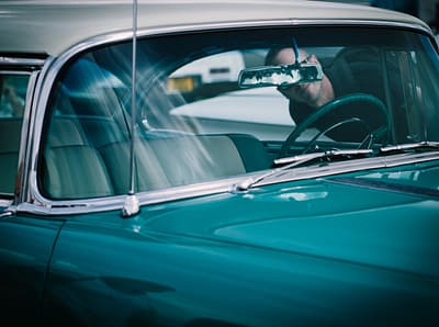 Close-up of a vintage car with a man visible in the rearview mirror, emphasizing classic and elegant design.