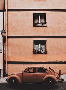 A classic Volkswagen Beetle parked along a rustic urban street with an old building backdrop.