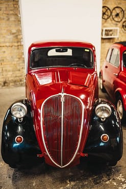 menu-06 Front view of a vintage red and black classic car in an indoor exhibition space.
