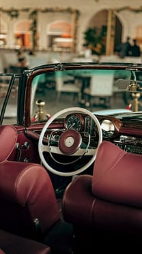 menu-14 Classic car interior featuring elegant red seats and a timeless steering wheel design in a cafe setting.