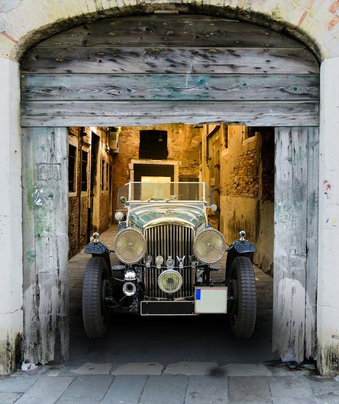 Vintage Bentley parked in a rustic alleyway showing classic automotive charm.